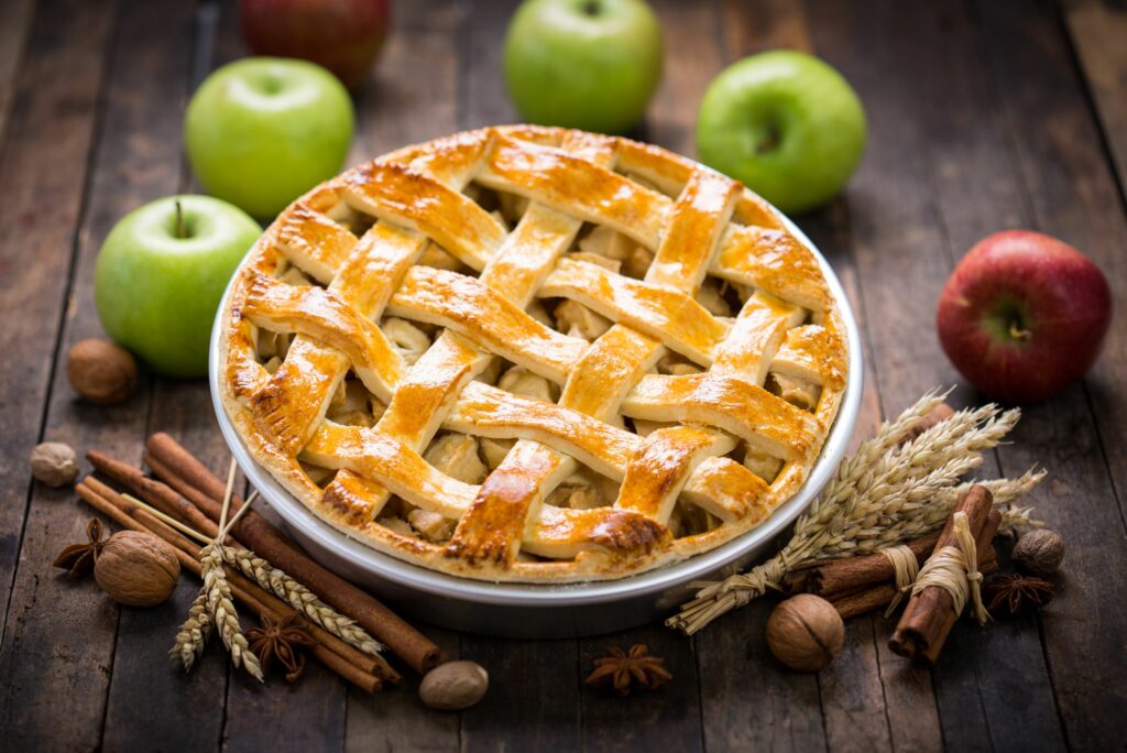 Golden lattice apple pie surrounded by apples, cinnamon sticks, and fall spices.