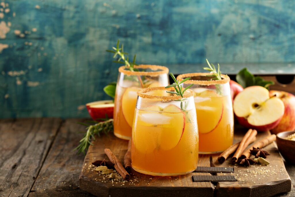 Apple cider made with fall fruit ingredients, garnished with cinnamon and rosemary on a rustic wooden table.