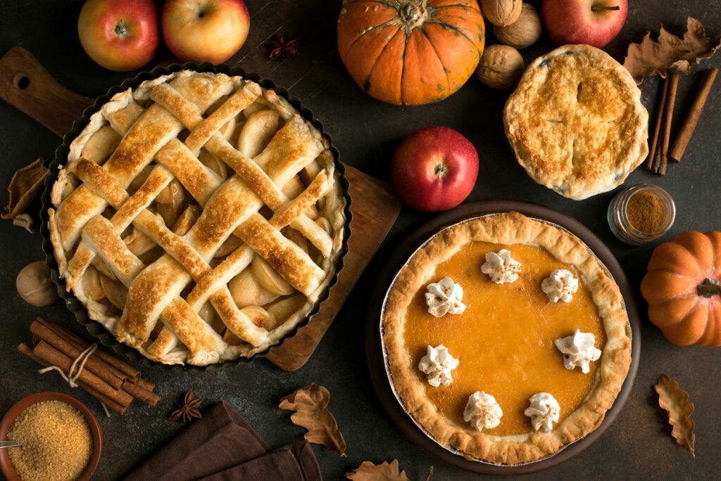 Freshly baked apple and pumpkin pies surrounded by autumn ingredients like apples, pumpkins, and cinnamon sticks.