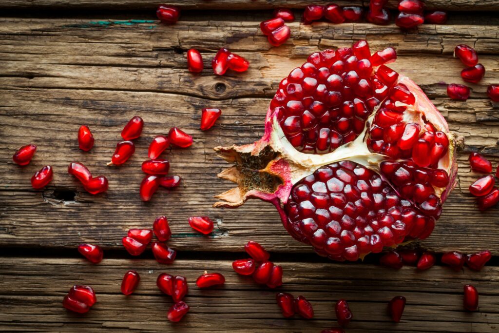 Ripe pomegranate split open on a wooden surface with seeds scattered around.