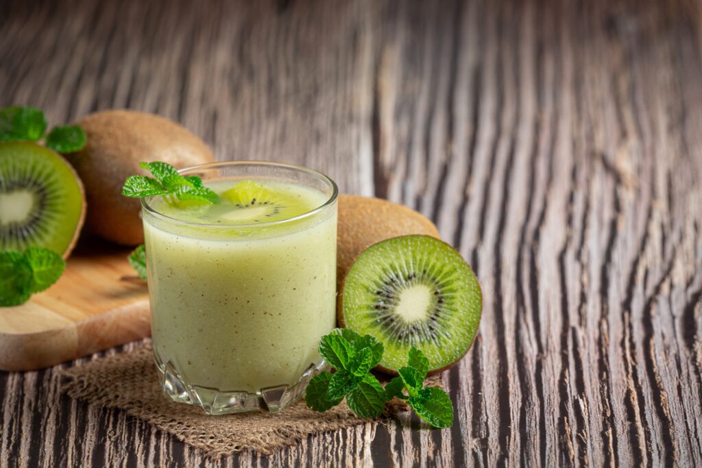 Fresh kiwi fruit beside a glass of processed kiwi purée or juice