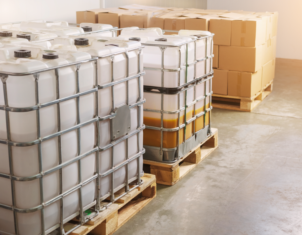 IBC totes in metal cages beside stacked cartons on wooden pallets in a warehouse